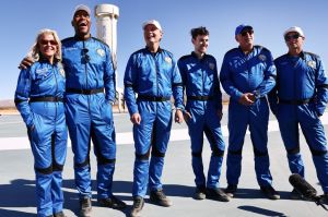 Six people wearing blue uniforms in front of a rocket.