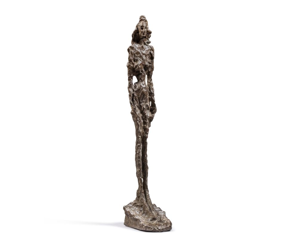 Bronze sculpture of a standing female figure with an elongated and textured form, created in Giacometti's signature style, against a white background.
