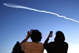 Two people take photos of a SpaceX rocket launch.
